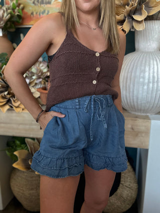 Woman wearing chambray blue ruffle hem shorts with an elastic drawstring waistband and side pockets