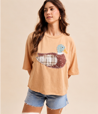 Woman wearing a camel Mallard Duck Patchwork Knit Top with plaid and floral duck appliqué and denim shorts.