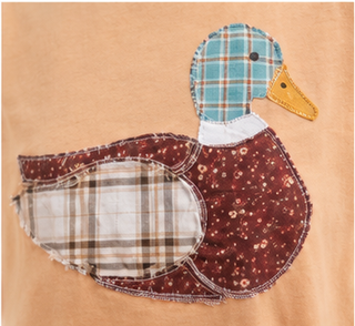 Woman wearing a camel Mallard Duck Patchwork Knit Top with plaid and floral duck appliqué and denim shorts.