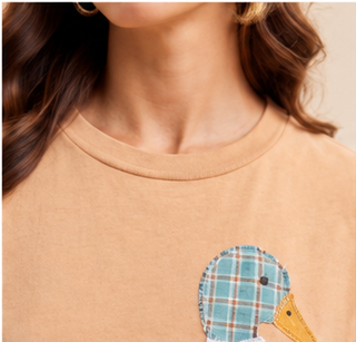 Woman wearing a camel Mallard Duck Patchwork Knit Top with plaid and floral duck appliqué and denim shorts.