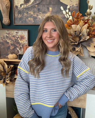 Woman wearing a dusty blue and cream striped sweater with yellow accents