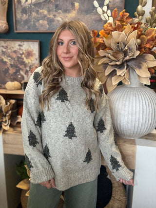 Woman wearing a heathered oatmeal-gray sweater with raised dark evergreen-tree motifs