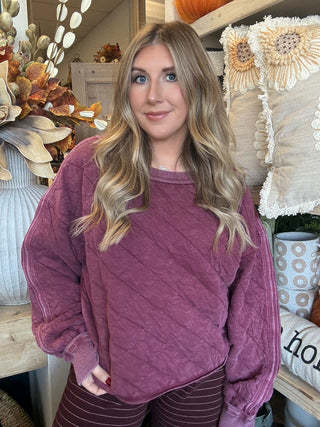 Woman wearing a washed wine quilted crew-neck sweatshirt with diagonal diamond stitching.