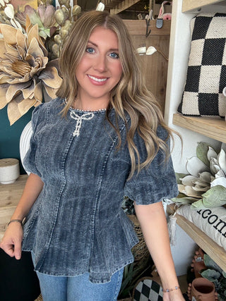 Woman wearing a washed-charcoal peplum top with puff sleeves and pearl bow neckline detail