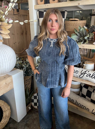 Woman wearing a washed-charcoal peplum top with puff sleeves and pearl bow neckline detail