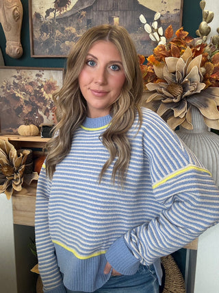 Woman wearing a dusty blue and cream striped sweater with yellow accents
