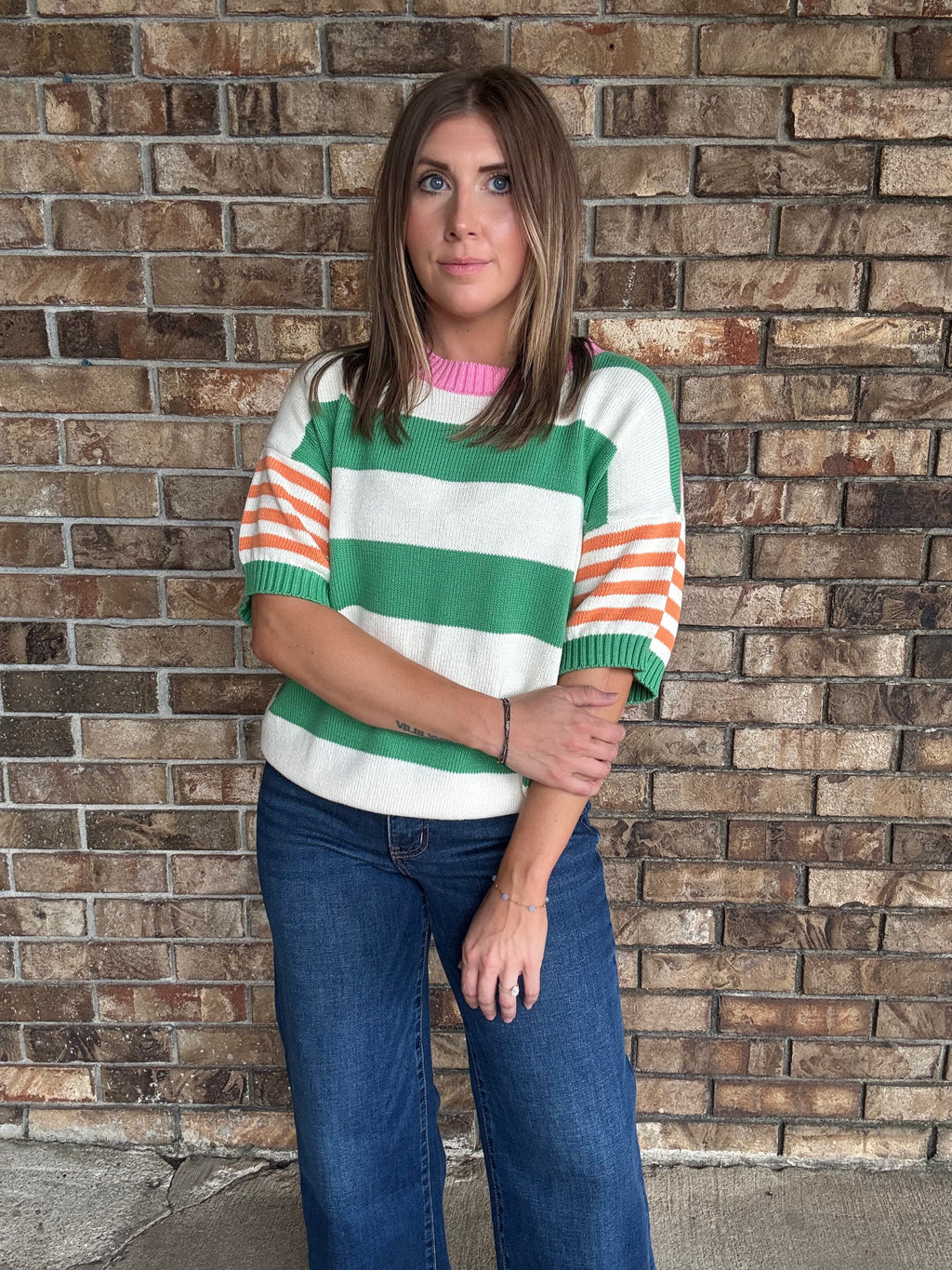 Woman wearing a green and ivory striped lightweight sweater with orange striped sleeves and pink neckline