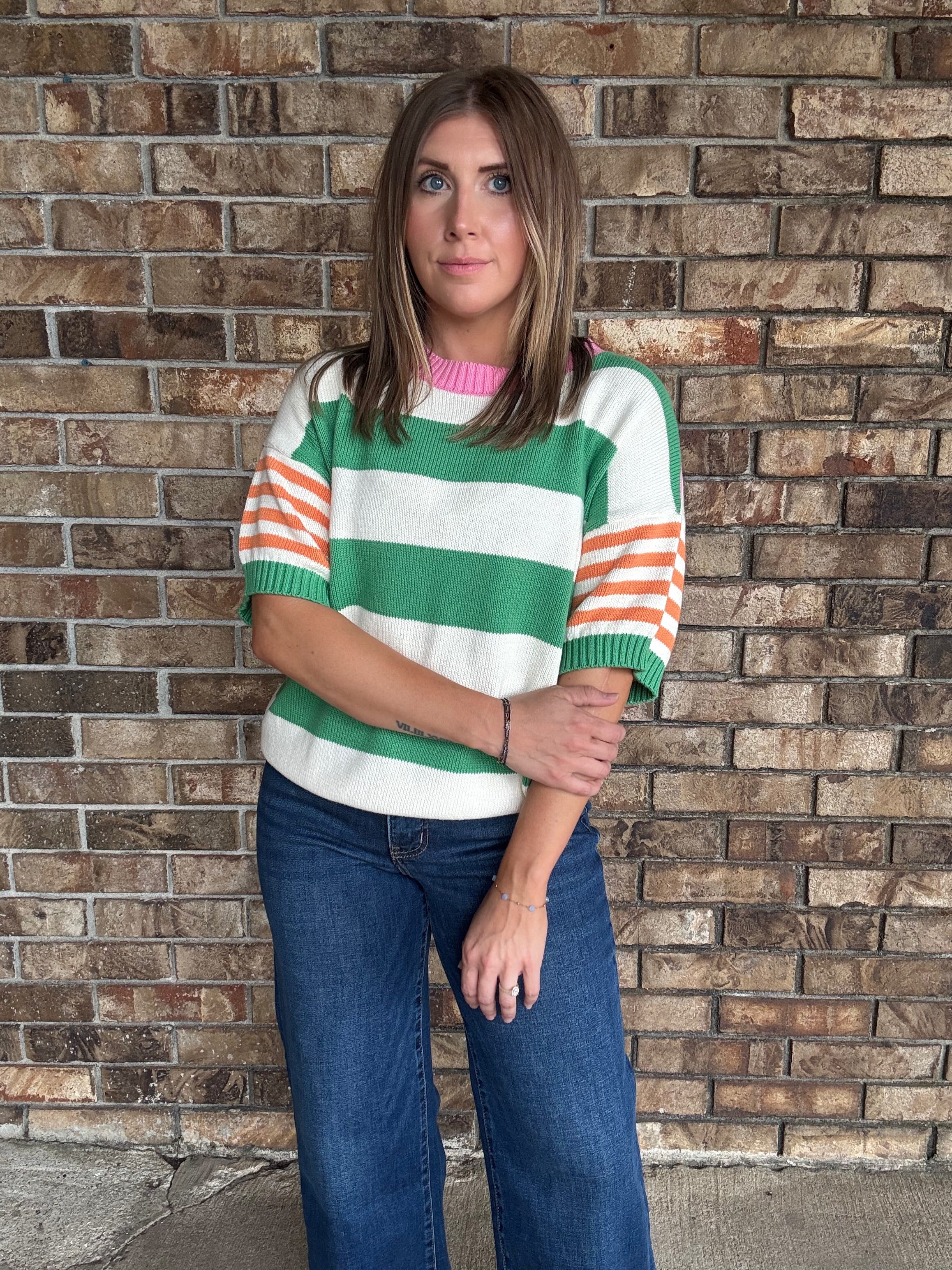 Woman wearing a green and ivory striped lightweight sweater with orange striped sleeves and pink neckline