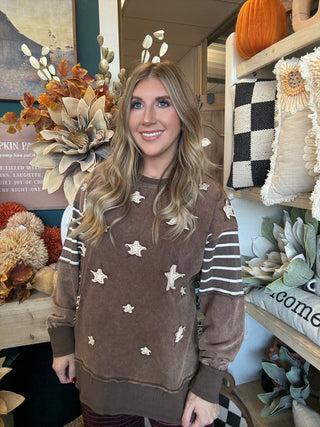 Woman wearing a chocolate vintage-wash pullover with cream appliqué stars and striped sleeves