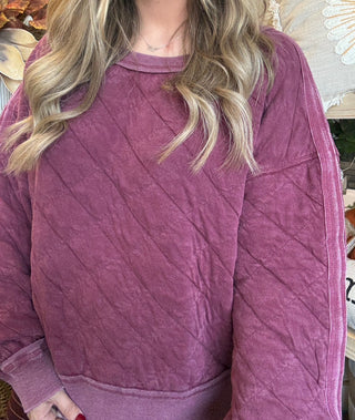 Woman wearing a washed wine quilted crew-neck sweatshirt with diagonal diamond stitching.