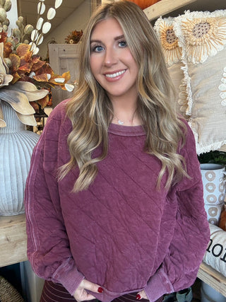 Woman wearing a washed wine quilted crew-neck sweatshirt with diagonal diamond stitching.