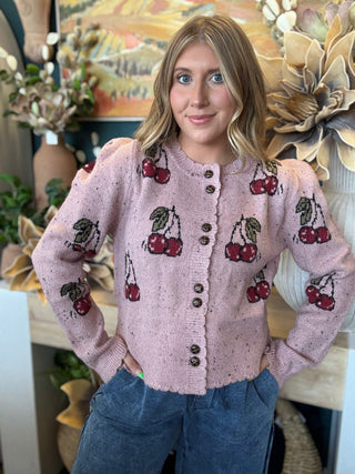 Woman wearing a dusty-pink cherry motif button-front cardigan from Pill Box Boutique