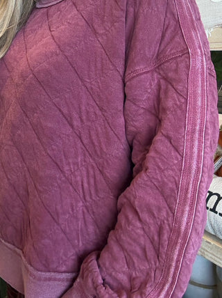 Woman wearing a washed wine quilted crew-neck sweatshirt with diagonal diamond stitching.