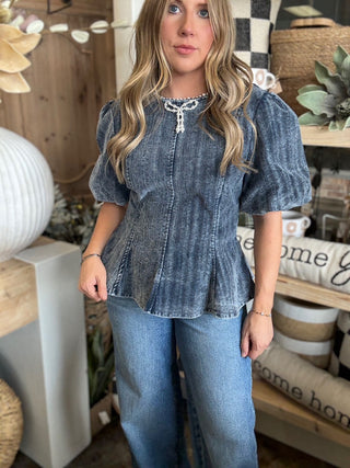 Woman wearing a washed-charcoal peplum top with puff sleeves and pearl bow neckline detail