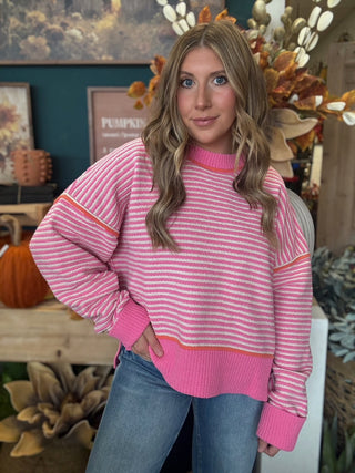 Woman wearing a pink-and-cream striped sweater with coral trim
