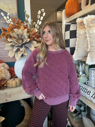 Woman wearing a washed wine quilted crew-neck sweatshirt with diagonal diamond stitching.