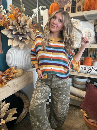 Woman wearing a mustard, cream, rust, forest green, light blue, and burgundy striped button-front sweater.