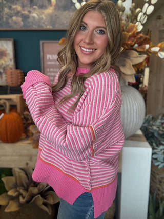 Woman wearing a pink-and-cream striped sweater with coral trim