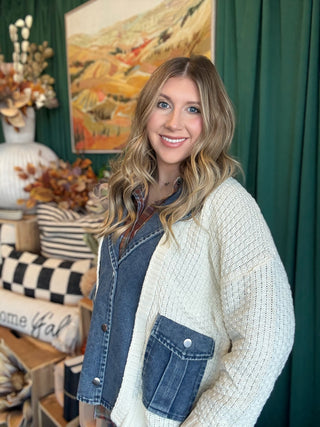 Woman wearing a cream open-knit twofer sweater with a washed-denim button front, flap pockets, and plaid collar accent.