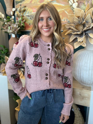 Woman wearing a dusty-pink cherry motif button-front cardigan from Pill Box Boutique