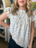 woman wearing cream and blue floral boutique blouse with ruffle neckline