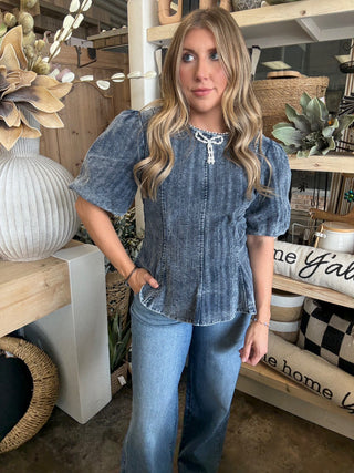 Woman wearing a washed-charcoal peplum top with puff sleeves and pearl bow neckline detail