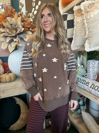 Woman wearing a chocolate vintage-wash pullover with cream appliqué stars and striped sleeves