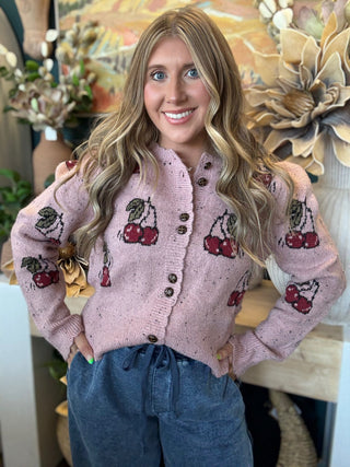 Woman wearing a dusty-pink cherry motif button-front cardigan from Pill Box Boutique