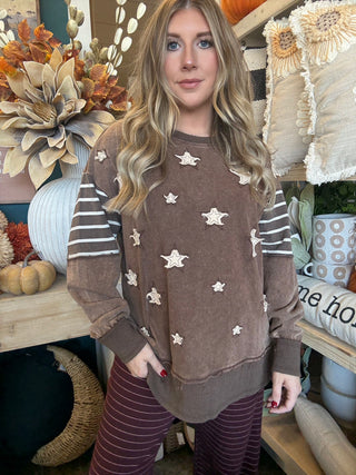 Woman wearing a chocolate vintage-wash pullover with cream appliqué stars and striped sleeves