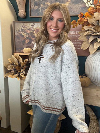 Woman wearing a speckled oatmeal sweater with embroidered flying mallards and rust-brown striped trim