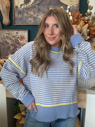 Woman wearing a dusty blue and cream striped sweater with yellow accents