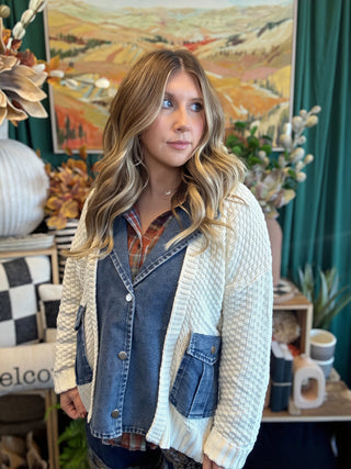 Woman wearing a cream open-knit twofer sweater with a washed-denim button front, flap pockets, and plaid collar accent.