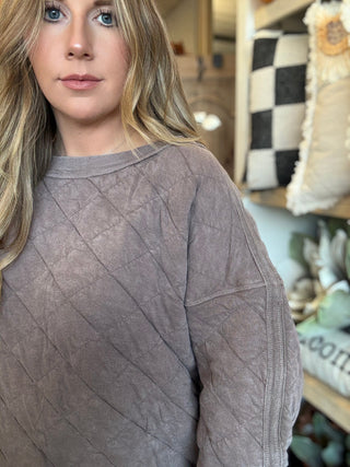 Woman wearing a washed-mocha quilted crew-neck pullover with diamond stitching and exposed seam details