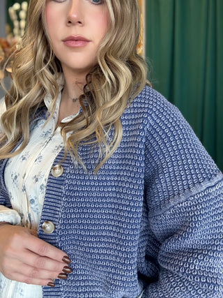 Woman wearing a denim-blue and ivory marled knit button-front cardigan with oversized buttons and dropped shoulders.