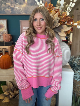 Woman wearing a pink-and-cream striped sweater with coral trim