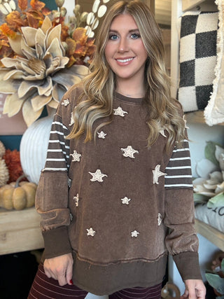 Woman wearing a chocolate vintage-wash pullover with cream appliqué stars and striped sleeves