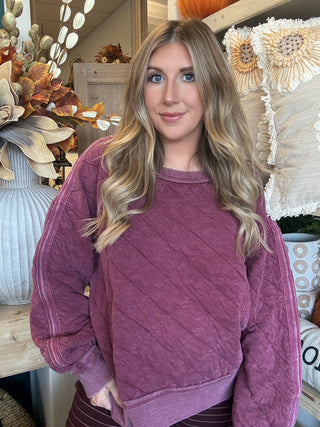 Woman wearing a washed wine quilted crew-neck sweatshirt with diagonal diamond stitching.