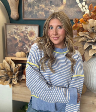 Woman wearing a dusty blue and cream striped sweater with yellow accents