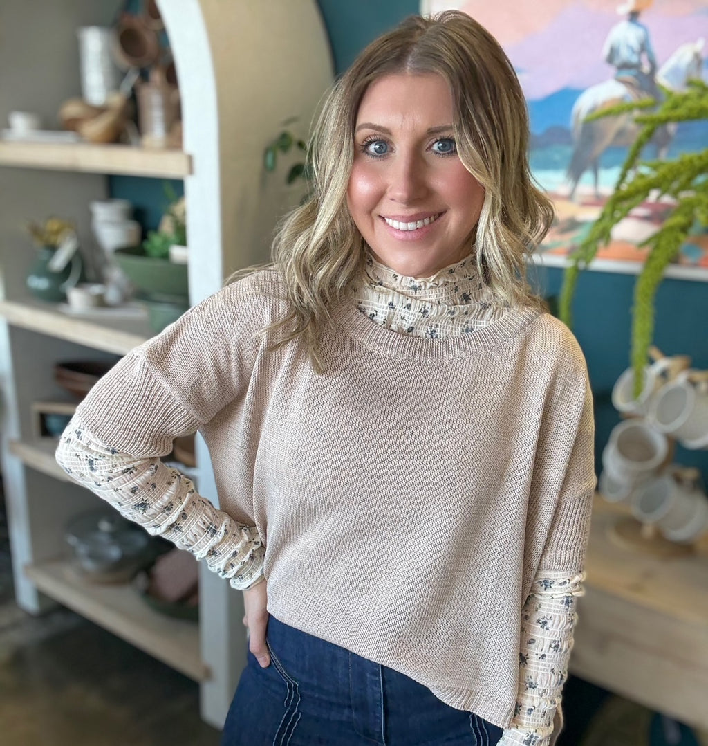 woman wearing oatmeal knit sweater layered over floral textured long sleeve top