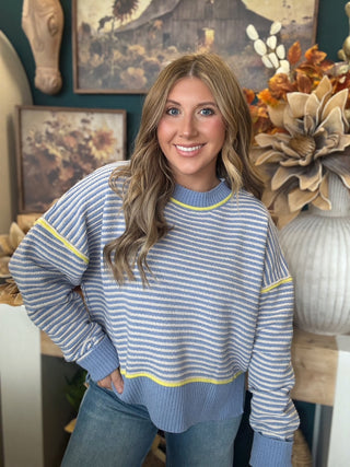 Woman wearing a dusty blue and cream striped sweater with yellow accents