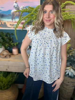 woman wearing cream and blue floral boutique blouse with ruffle neckline