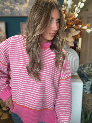 Woman wearing a pink-and-cream striped sweater with coral trim