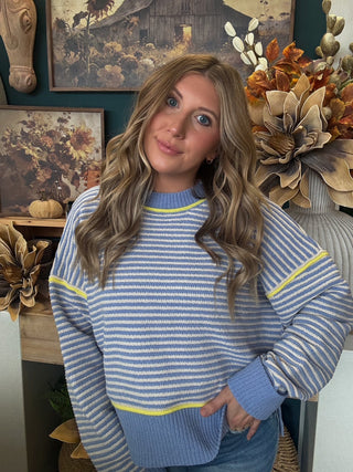 Woman wearing a dusty blue and cream striped sweater with yellow accents