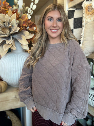 Woman wearing a washed-mocha quilted crew-neck pullover with diamond stitching and exposed seam details