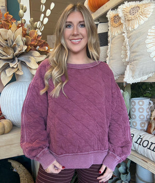 Woman wearing a washed wine quilted crew-neck sweatshirt with diagonal diamond stitching.