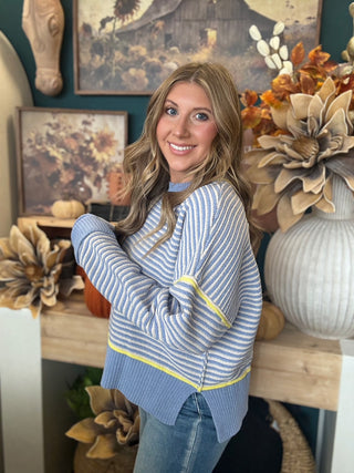 Woman wearing a dusty blue and cream striped sweater with yellow accents