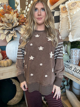 Woman wearing a chocolate vintage-wash pullover with cream appliqué stars and striped sleeves