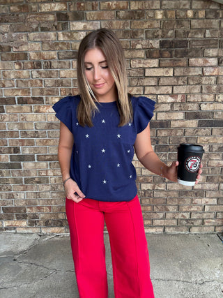 Woman wearing a navy star embroidered ruffle sleeve sweater top with lightweight knit fabric