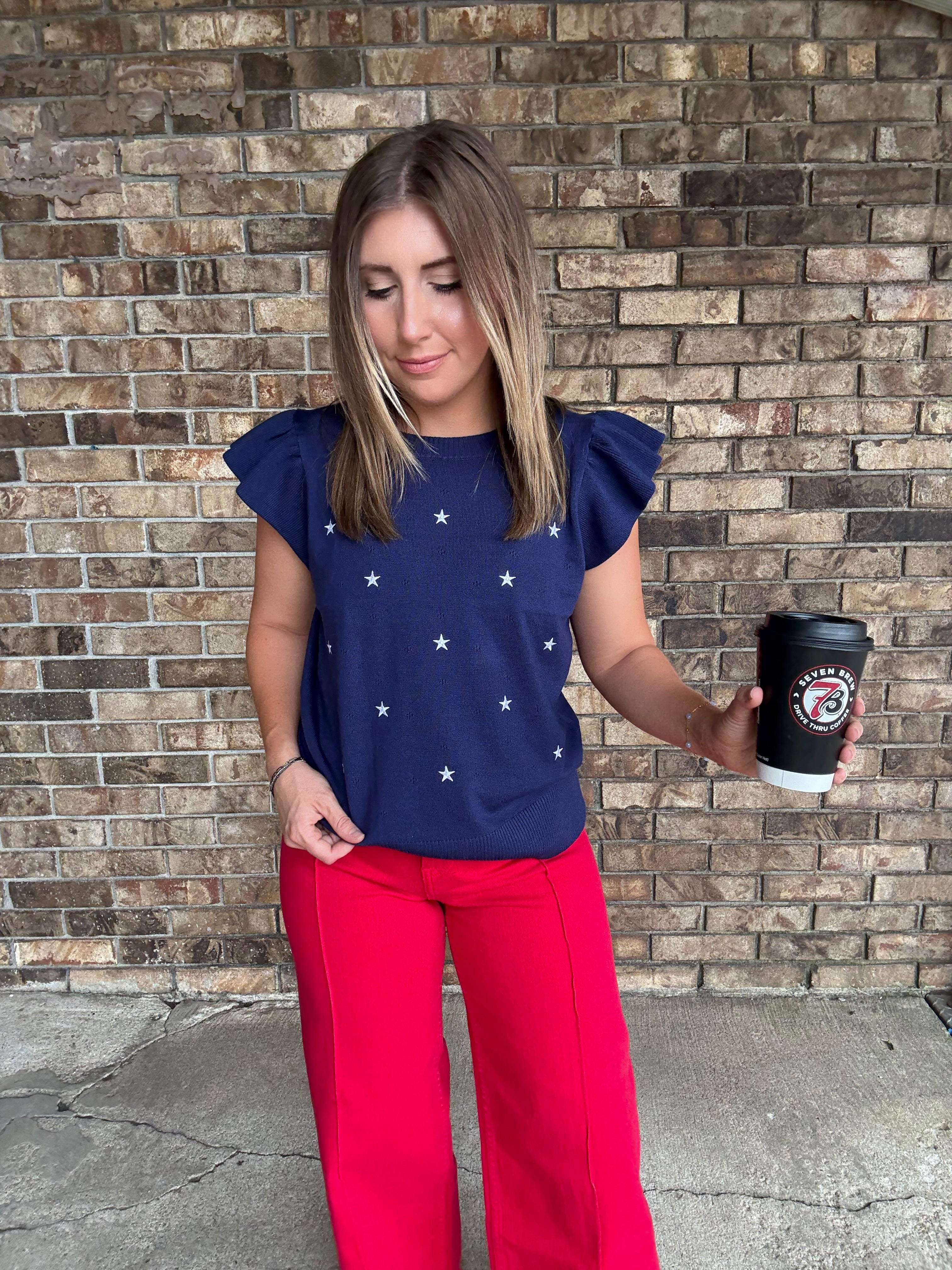 Woman wearing a navy star embroidered ruffle sleeve sweater top with lightweight knit fabric