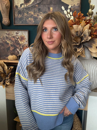 Woman wearing a dusty blue and cream striped sweater with yellow accents